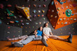 © anatoliy_gleb - Three tired climbers with closed eyes sitting on the orange mat near rock wall indoors. Bouldering