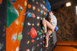 © anatoliy_gleb - Strong guy climbing up on practice wall in gym, making difficult motion, side view. Bouldering