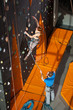 © anatoliy_gleb - Athletic girl climbing on an indoor rock-climbing wall and man standing on the ground insuring the climber