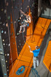 © anatoliy_gleb - Athletic female climber is climbing on an indoor rock-climbing wall and male belayer standing on the ground insuring the climber