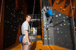 © anatoliy_gleb - Man stands on the ground near rock wall indoors, looking at the camera and insuring the climber, using rope and belay device