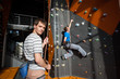 © anatoliy_gleb - Man stands on the ground near rock wall indoors, looking at the camera and insuring the climber