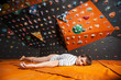 © anatoliy_gleb - Tired male climber with closed eyes lying on the orange mat near rock wall indoors. Bouldering