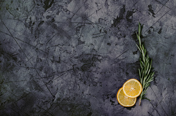 Rosemary with sliced lemon on dark stone table