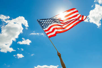 USA flag in hand with beautiful white clouds and blue sky on background