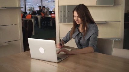 Poster - Young happy woman sitting at the working place. Wearing in elegant grey dress. Redhead caucasian model. Female works at her office. 