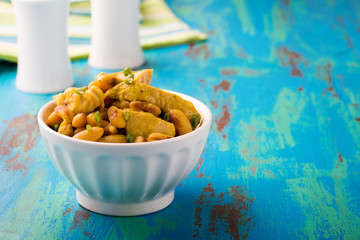 Canvas Print - Chicken with white beans in a curry sauce on a blue wooden board