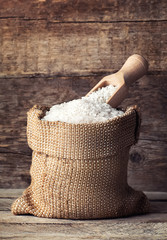 Wall Mural - rice in burlap sack with scoop on wooden background