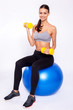 Staying fit. Young beautiful woman in sportswear with perfect bodie doing exercise with dumbbells and looking at camera with smile while sitting on fitness balls over white isolated background.
