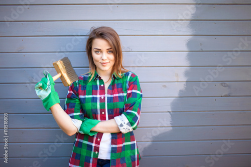 Fotografía Young working woman with paint brush, freshly painted wooden exterior wall behin
