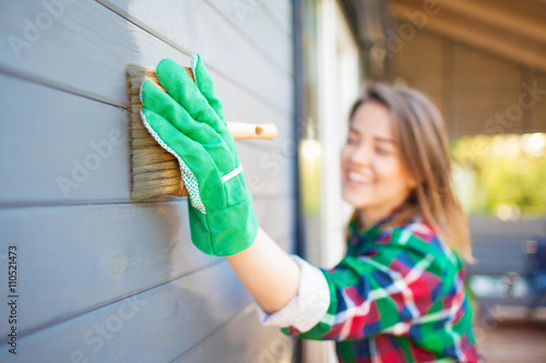 Fotomural Cheerful woman applying protective varnish or paint on wooden house tongue and groove cladding elevation wall