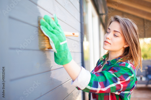 Cuadros en Lienzo Young woman applying protective varnish or paint on wooden house tongue and groove cladding elevation wall