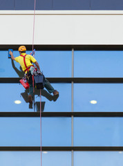 Alpinist worker washing windows of the modern building