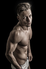 Wall Mural - Lean athletic shirtless young man standing on dark background