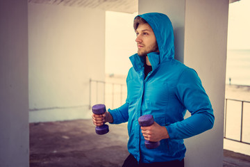 Wall Mural - A man in a blue hoodie exercising with dumbbells.