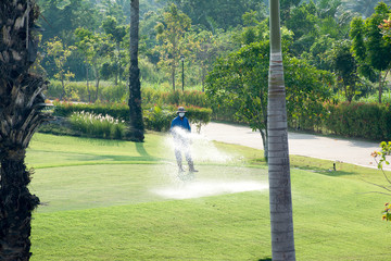 Worker is watering the grass in the golf course.