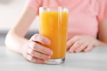 Sticker - Female hand holding glass of orange juice on wooden table closeup