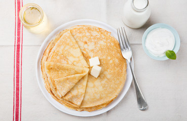 Wall Mural - Thin crepes or pancakes with butter, honey and sour cream on a rustic textile background Top view