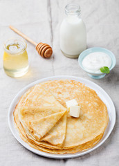 Wall Mural - Thin crepes or pancakes with butter, honey and sour cream on a rustic textile background