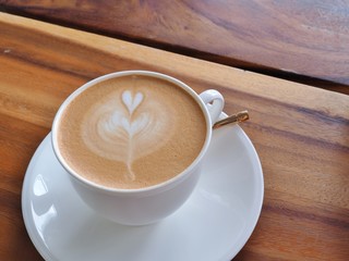 A cup of latte art coffee with heart pattern in a white cup on wooden background.