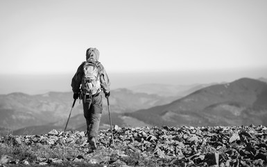 male sportsman backpaker walking on the rocky top of the mountain with beautiful mountains on backgr