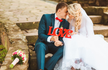 Young couple on the stairs in the park. They are and looking into each other's eyes. Wedding session in the park. Bride and groom with bubble and a sign with the words love