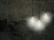 Close-up Of Three White Turned On Light Bulbs Against Dark Gray Concrete Wall Background