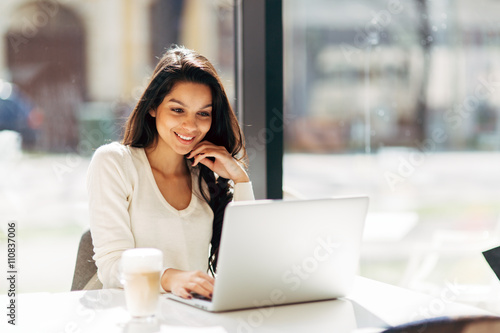 Brunette utilisant un ordinateur portable dans le café Poster Mural XXL