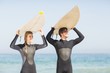 © WavebreakmediaMicro - Happy couple in wetsuit carrying surfboard over head