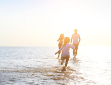 Happy Young Family Having Fun Running On Beach At Sunset