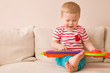 Portrait of adorable toddler boy sitting on the sofa and playing toy piano. Early learning at home. Little musician. Child and toys.Education. Indoors.