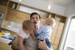 © Connect Images - Father struggling to carry male and female twin toddlers in dining room