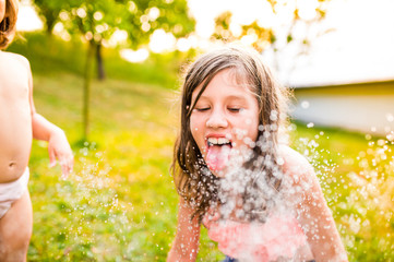 Two girls at the sprinkler, sunny summer in the garden