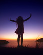 Silhouette of happy child girl stands on background of sunset sky and sea and throws his hands as if flies