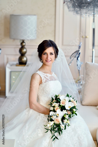 Beauty Bride In Bridal Gown With Bouquet And Lace Veil Indoors