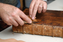 Close Up Of Hands Of Senior Male Traditional Bookbinder Removing Leather From Book