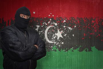 Wall Mural - dangerous man in a mask standing near a wall with painted national flag of libya