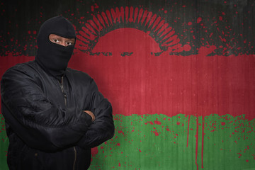 Wall Mural - dangerous man in a mask standing near a wall with painted national flag of malawi