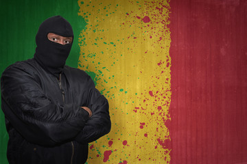 Wall Mural - dangerous man in a mask standing near a wall with painted national flag of mali