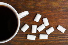 White Cup With Strong Coffee And White Chewing Gum In The Form Of Cushions On Brown Wooden Background