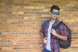 © GENETTICA - Young man with sunglasses and shirt carrying a bag. He is standi