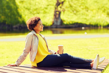 Wall Mural - happy african woman drinks coffee at summer park 