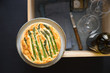Asparagus tart with egg and cheese filling on wooden box with glasses and wine bottle prepared for picnic. Selective focus on the tart surface.