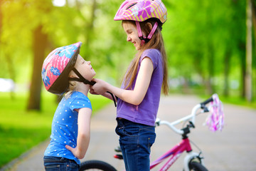 Adorable girl helping her sister to put a bicycle helmet on