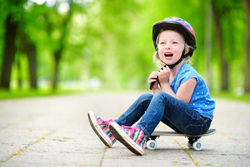 Cute little preteen girl wearing helmet sitting on a skateboard