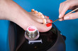 pedicure process macro closeup. Master manicurist gets a red gel on the nail model. Photo on blue background. 