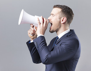 Handsome businessman shouting by megaphone on grey background