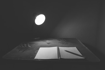 notebook and pencil on a desk in the light of lamp. Black and Wh