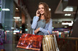 © mikhail_kayl - Beautiful girl with curly hair talking on mobile phone. Fashion Shopping Girl Portrait. Beauty Woman with Shopping Bags in Shopping Mall. Shopper. Sales. Shopping Center