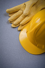 Yellow hard hat leather protective gloves on grey background con